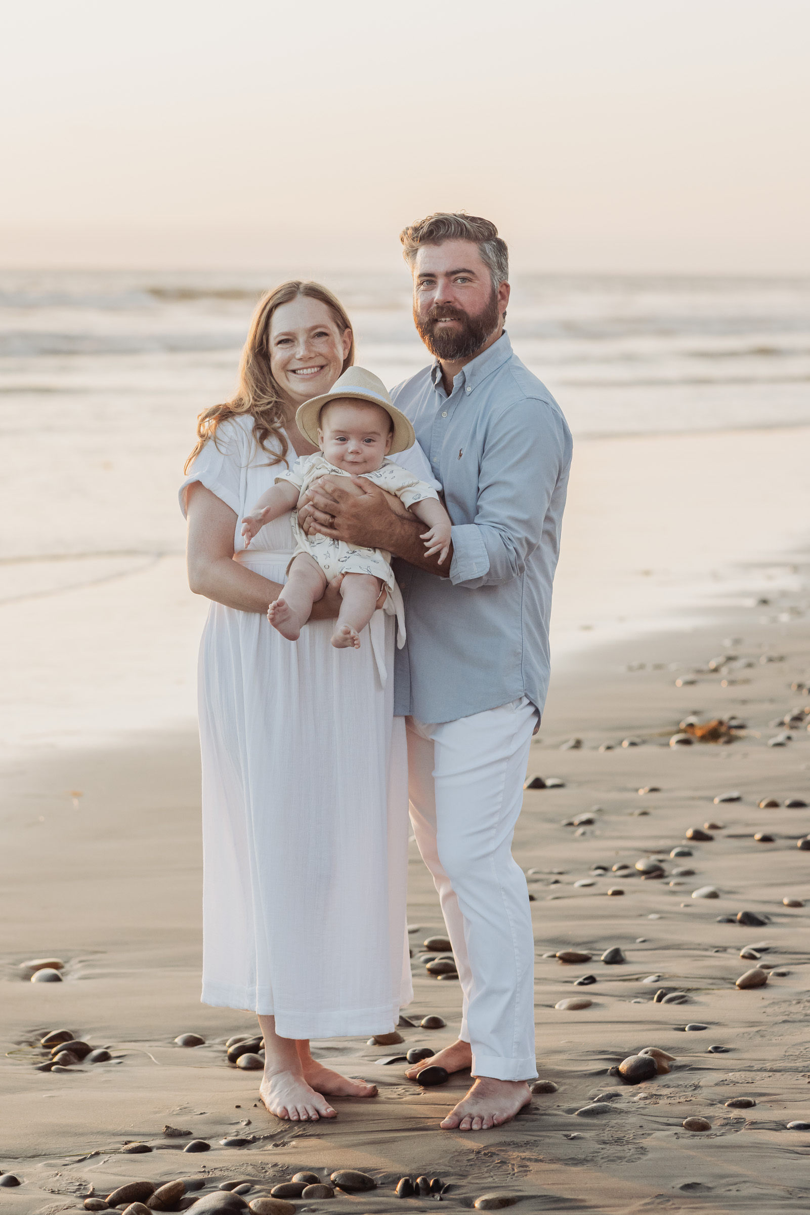 Parents holding their swaddled newborn on the beach in Carlsbad, San Diego