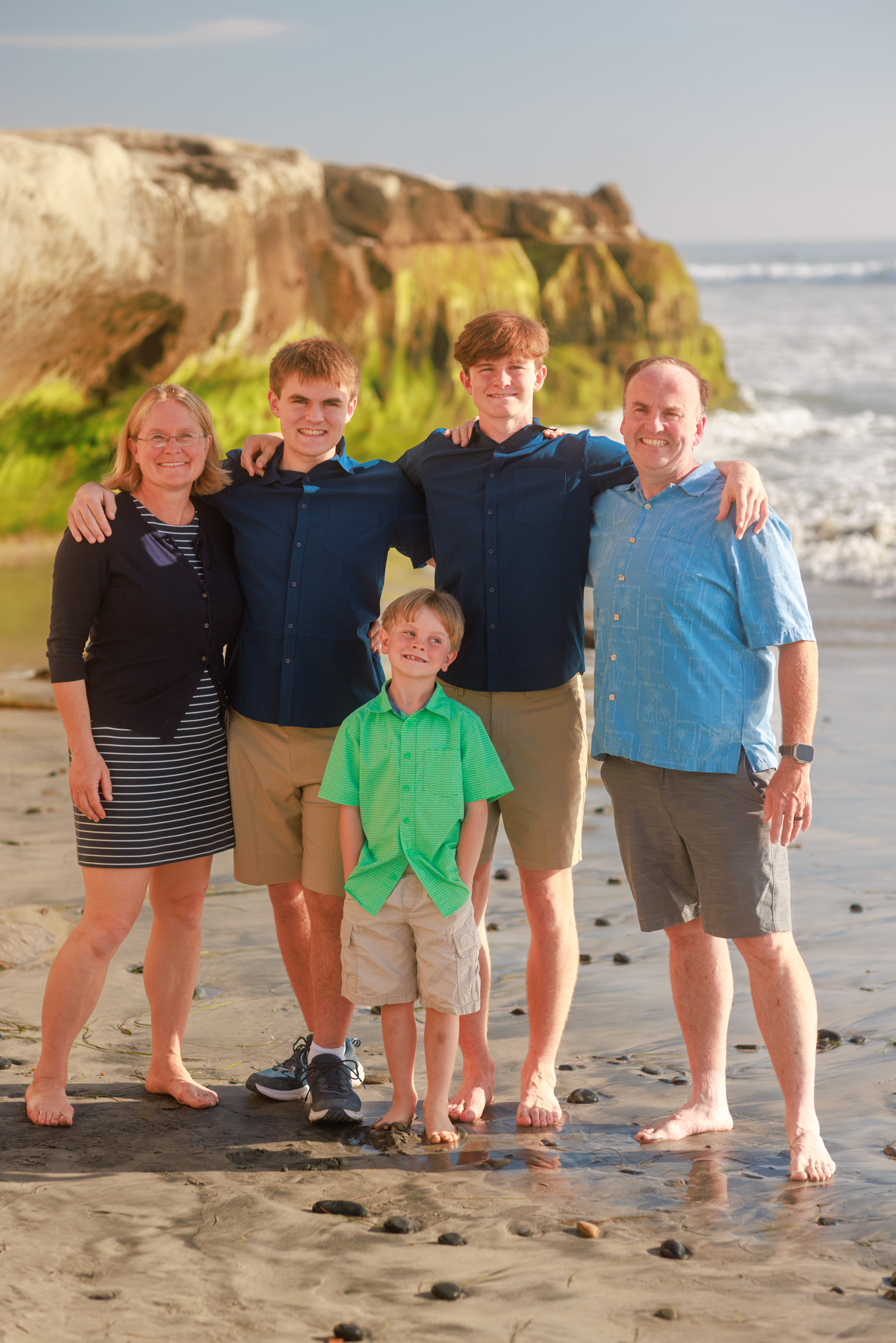 Five family members pose together below the Carlsbad sandstone bluffs, with open sky and ocean behind them.