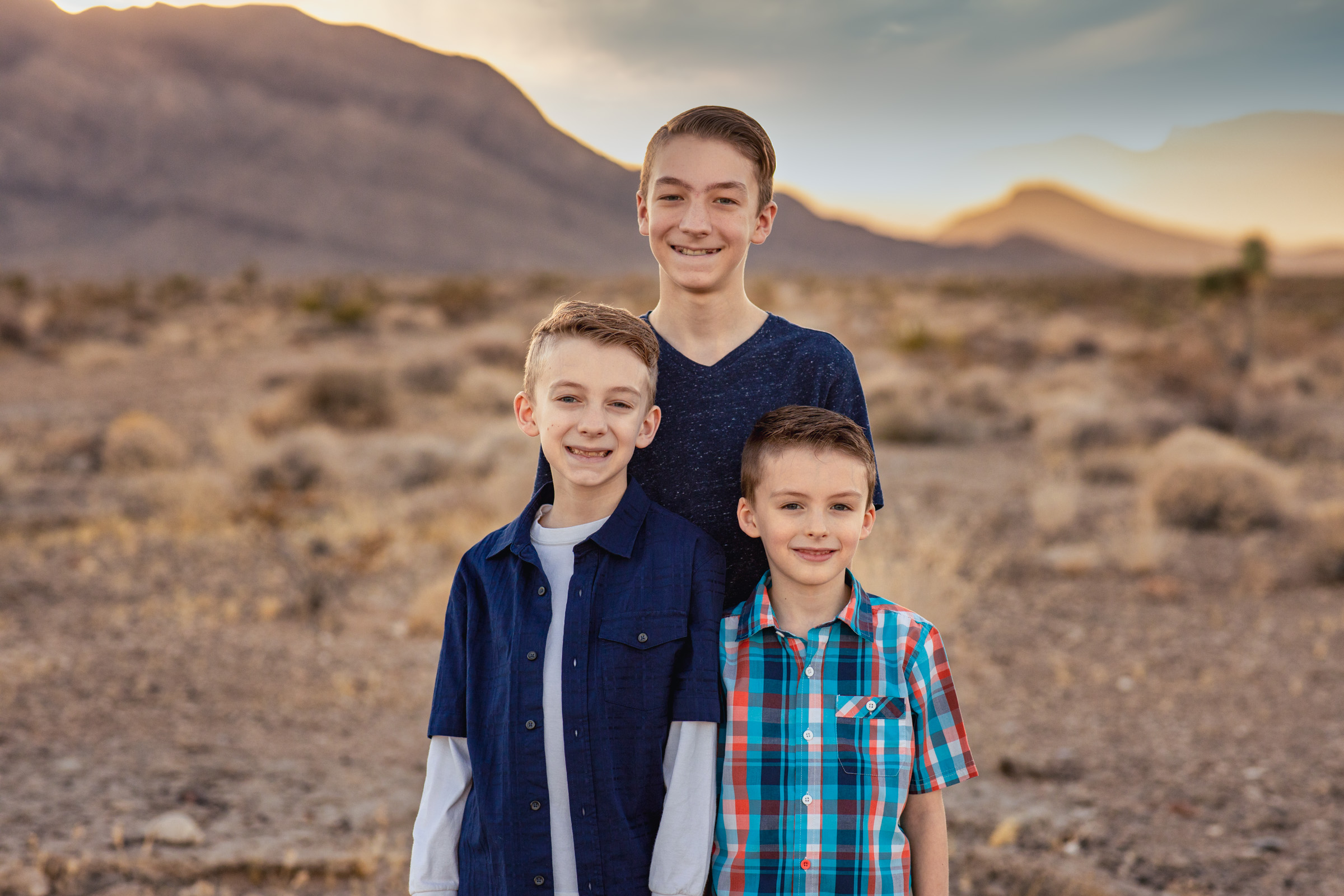 Three brothers of different ages standing together and smiling with desert mountains behind them
