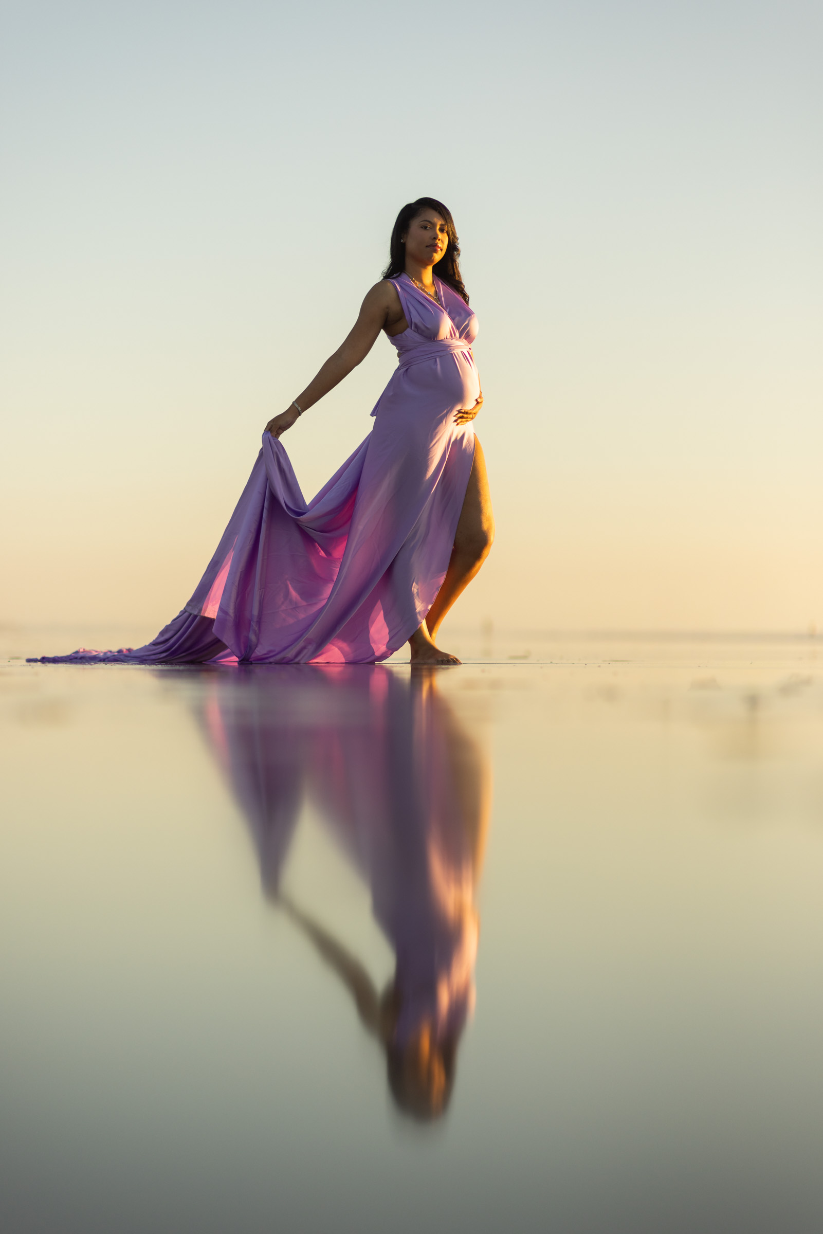 Expecting mother in a flowing gown reflected on the wet sand in Carlsbad at sunset
