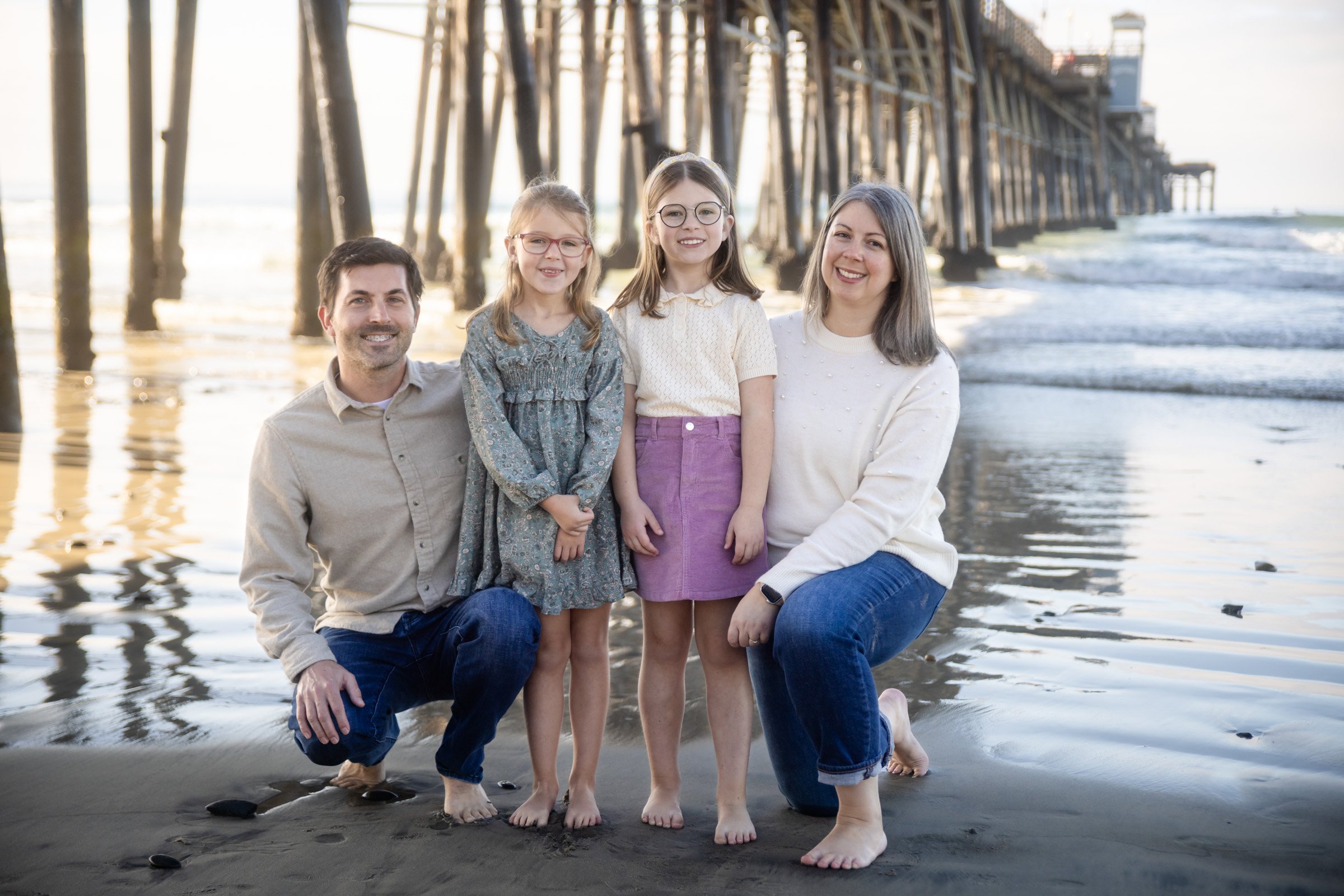 Family standing among the pier pilings at sunset in Oceanside, San Diego County