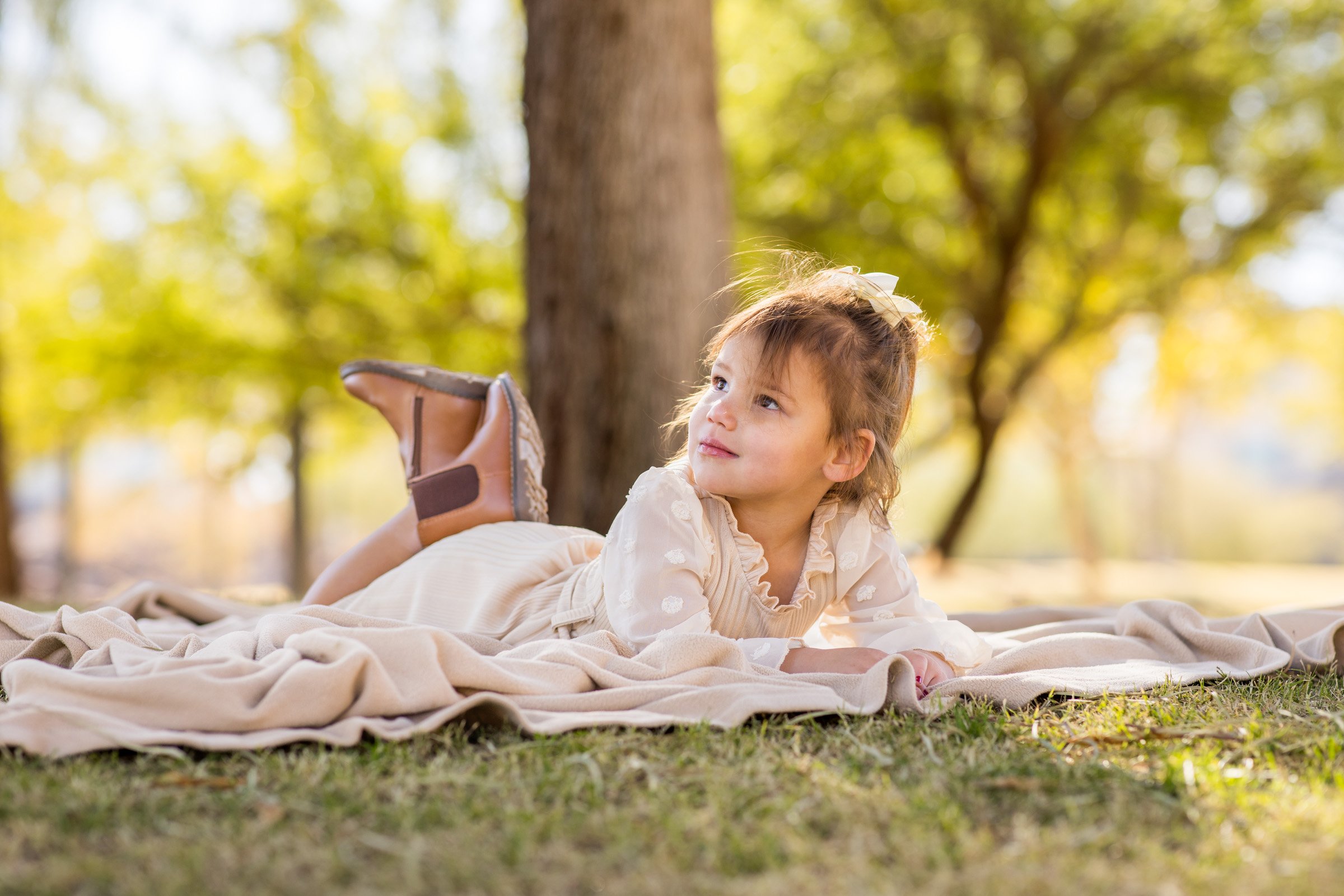 Little girl resting on a blanket under a shade tree in a Henderson park