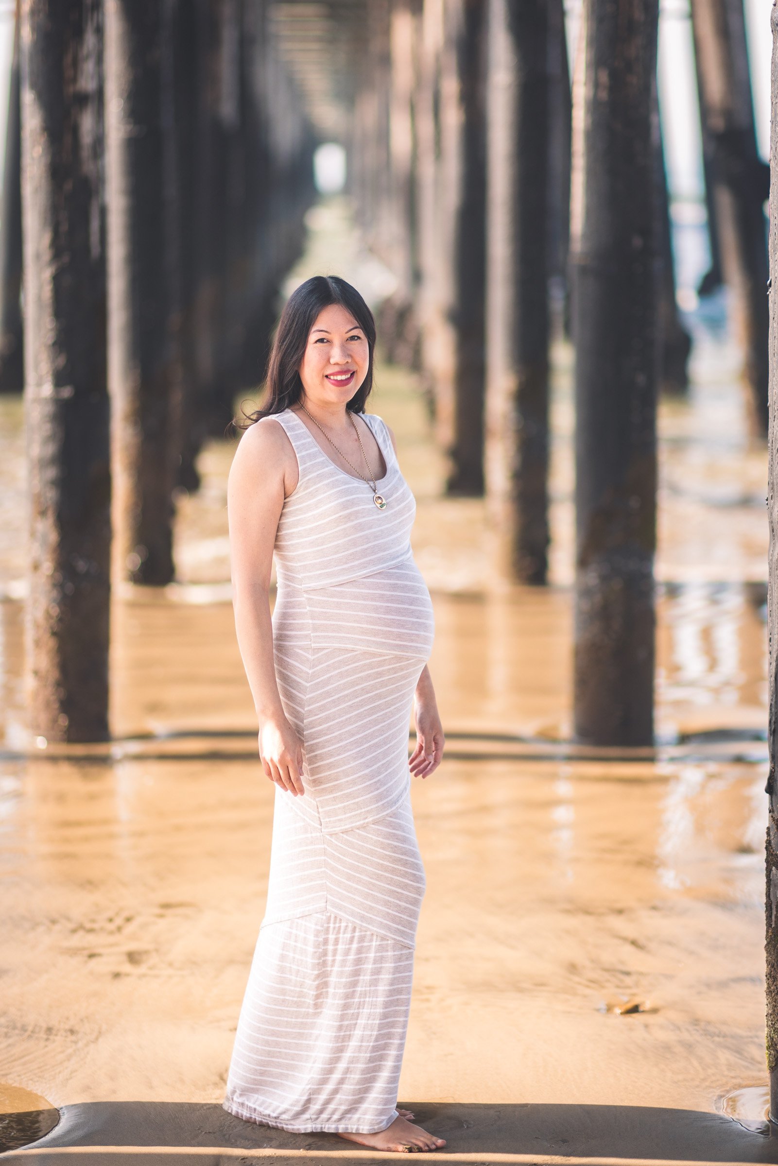 Expecting mother in warm light beneath the Oceanside pier in San Diego County