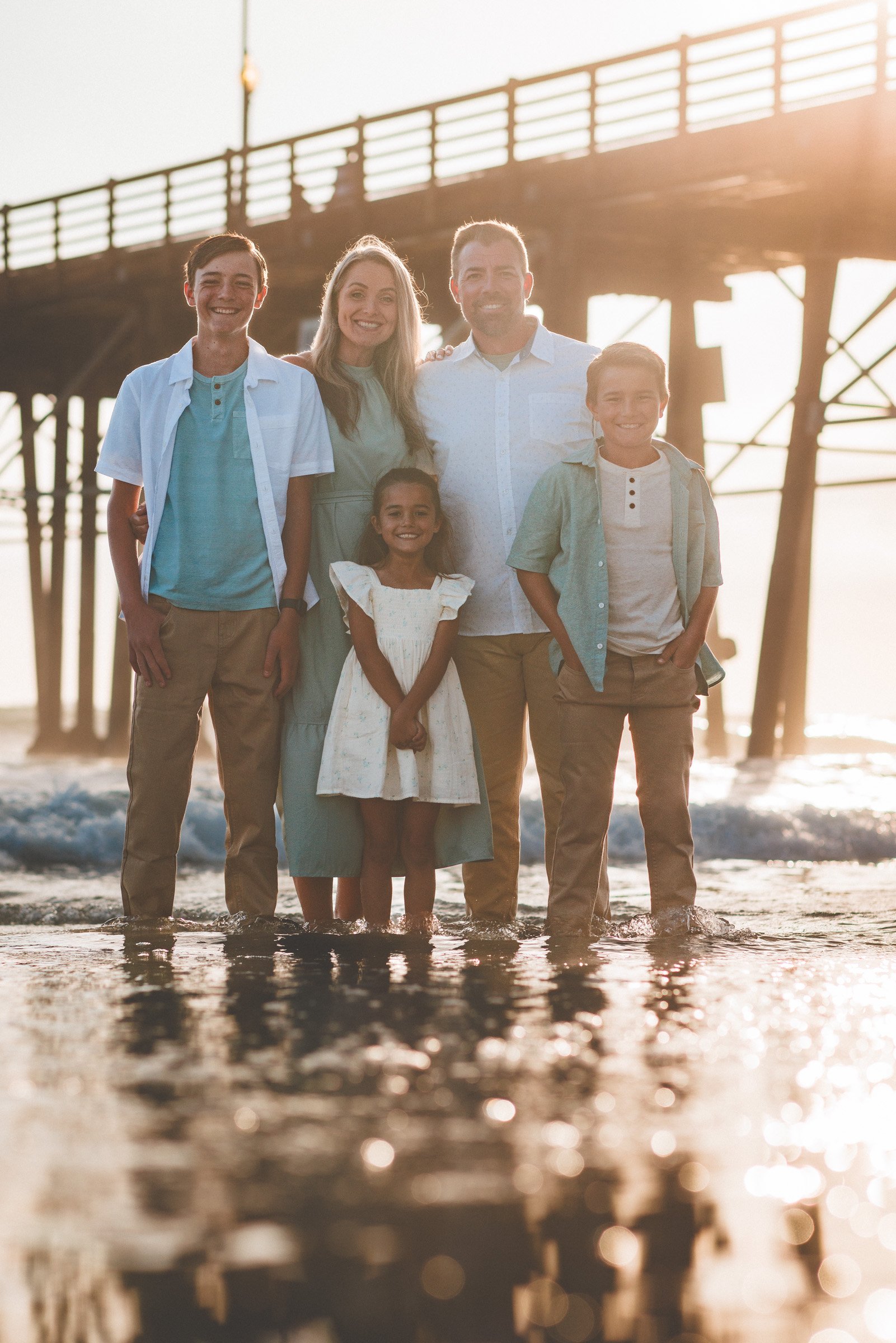 Family on the sand beside the Oceanside pier at sunset in San Diego County